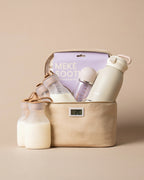 A beige fabric chiller bag filled with baby bottles, a bottle warmer, and a milk warmer, set against a solid beige background. The brand name 'MEKE' is visible on the packaging.