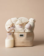 A beige fabric chiller bag filled with baby bottles, a bottle warmer, and a milk warmer, set against a solid beige background. The brand name 'MEKE' is visible on the packaging.