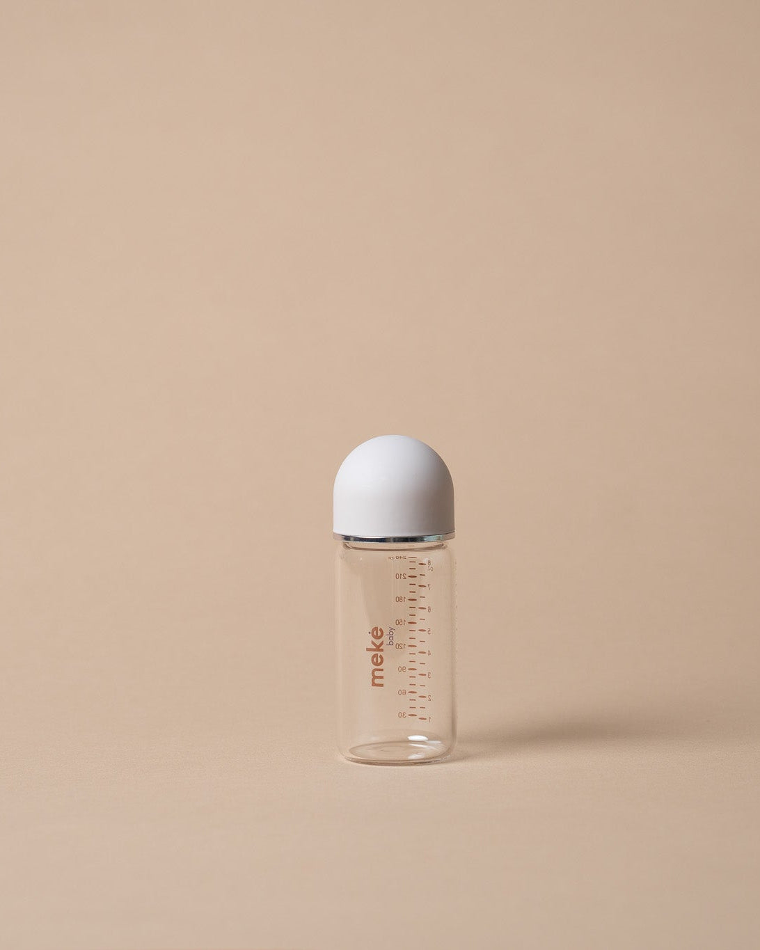 A small clear baby bottle with a white cap, standing upright on a warm beige background. The bottle has red measurement markings and the brand name 'miso' printed vertically on the side.