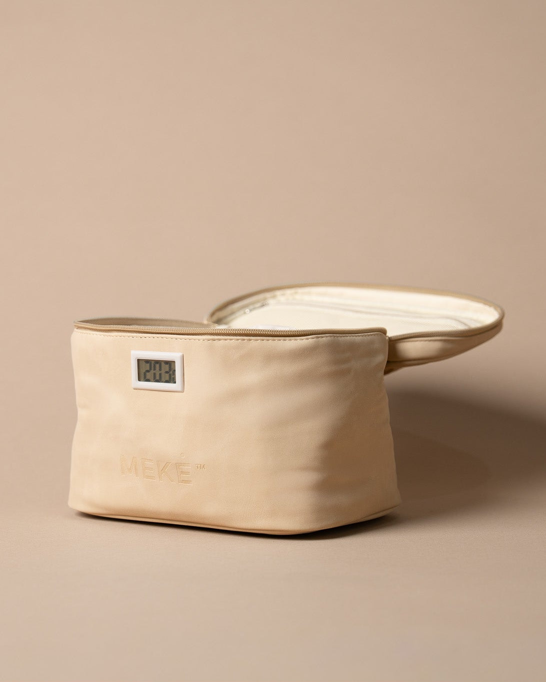 A cream coloured canvas milk pouch with a small digital temperature indicator window and embossed brand name, shown next to its matching lid on a solid beige background.