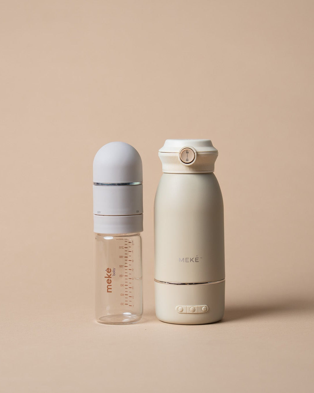 Two minimalist baby feeding essentialsi ncluding bottle and milk warmer a soft warm beige and off-white colorway, standing side by side on a solid beige background. The left bottle is clear with a white cap and a white collar, featuring red 'make' branding.