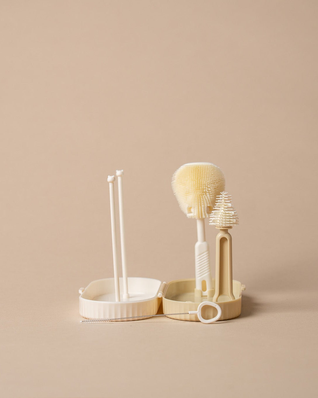 A set of three cream-colored plastic cleaning tools, including a small brush, a scrubber, and a stand with two applicator sticks, arranged on a solid beige background.