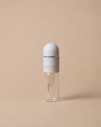A small clear glass baby bottle with a white cap and a white collar, featuring red measurement markings and the brand name 'miso' printed on the side, set against a solid beige background.