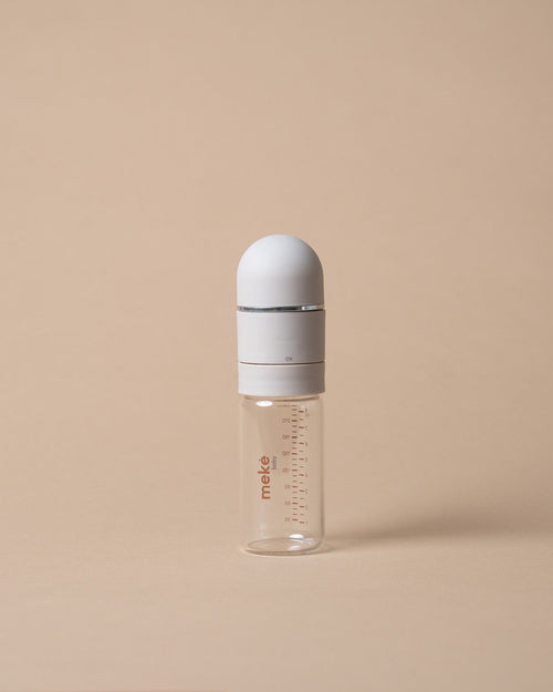 A small clear glass baby bottle with a white cap and a white collar, featuring red measurement markings and the brand name 'miso' printed on the side, set against a solid beige background.