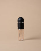 A clear plastic baby bottle with measurement markings and a matte black cap, standing upright on a solid beige background.