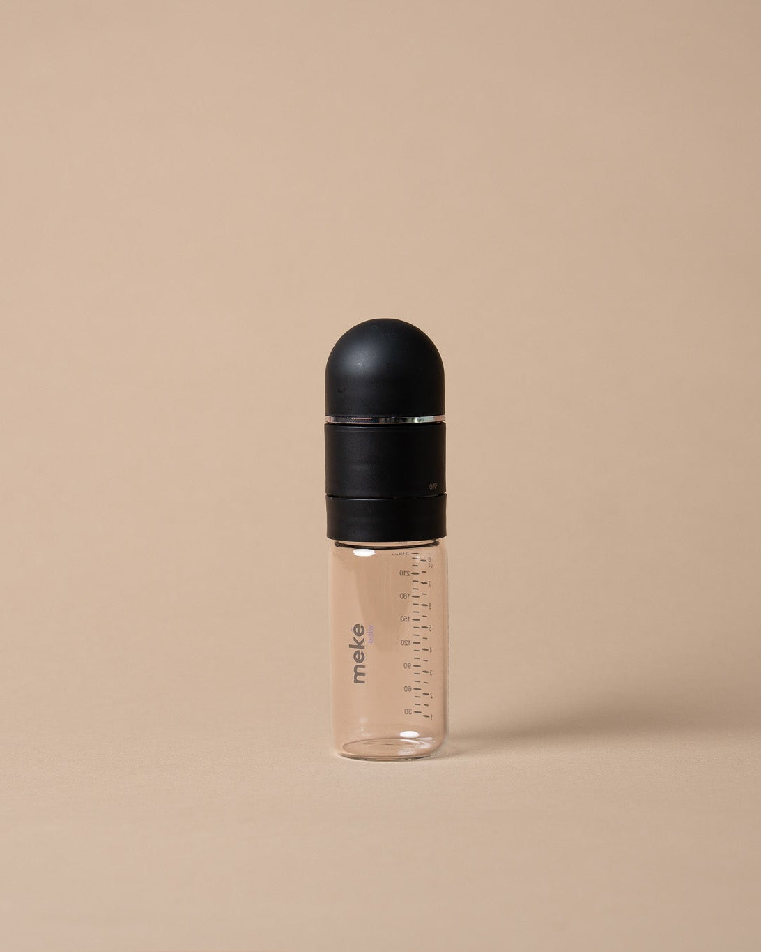 A clear plastic baby bottle with measurement markings and a matte black cap, standing upright on a solid beige background.