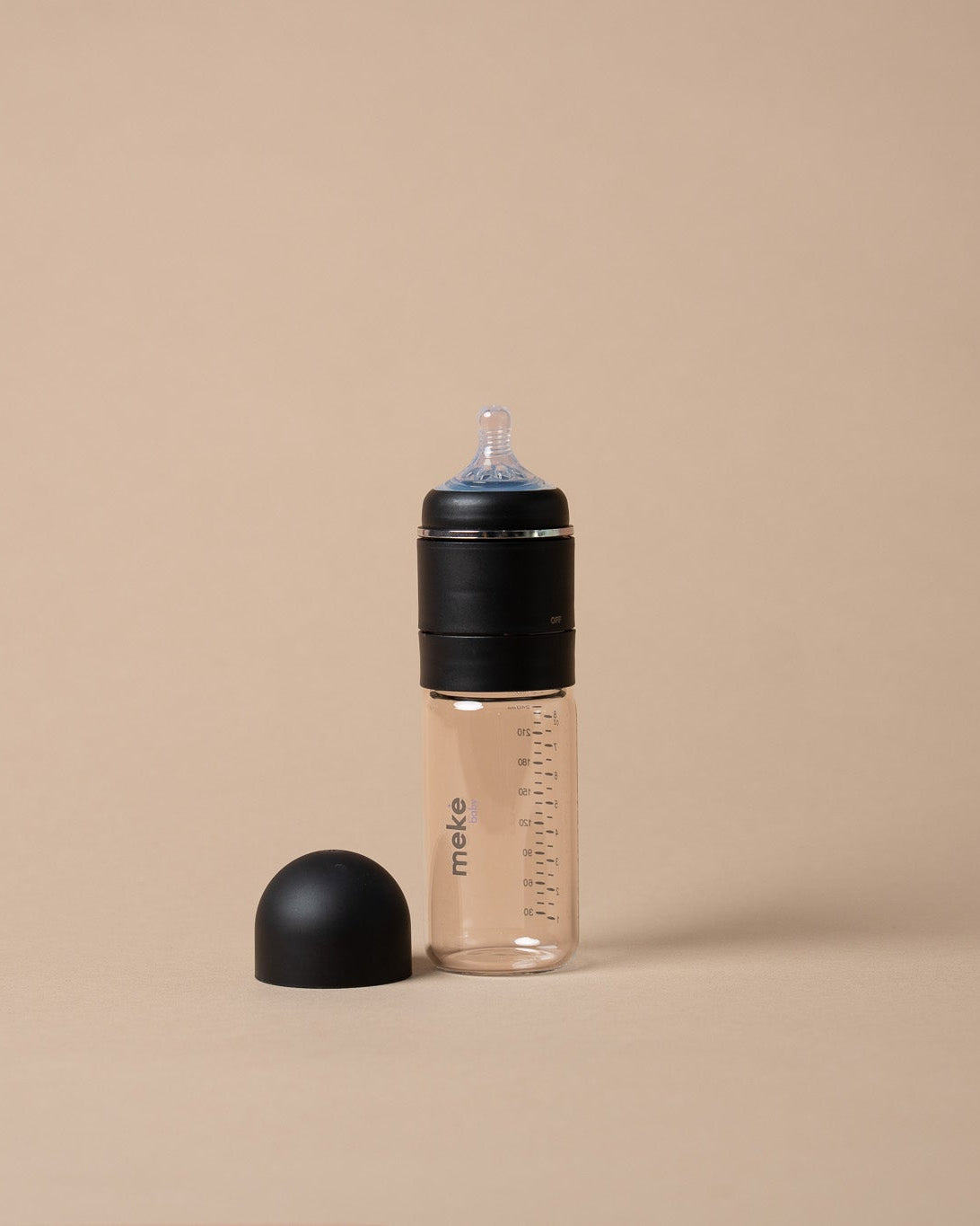 A clear plastic baby bottle with a black cap and a black silicone nipple shield, shown on a solid beige background.