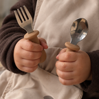 Toddler holding the travel feeding kit fork and spoon while wearing the bib